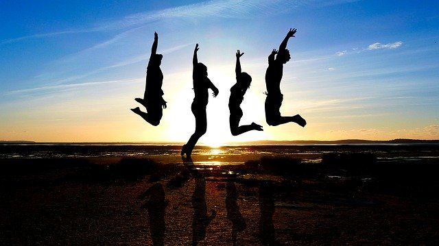 夕日をバックに海でジャンプする4人の人