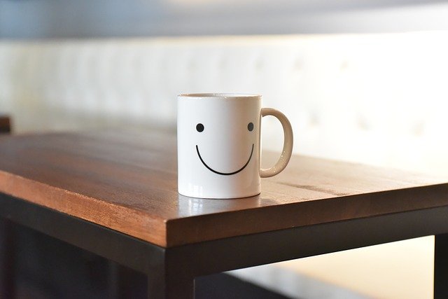 机の隅に置かれた笑った顔の書かれたマグカップ