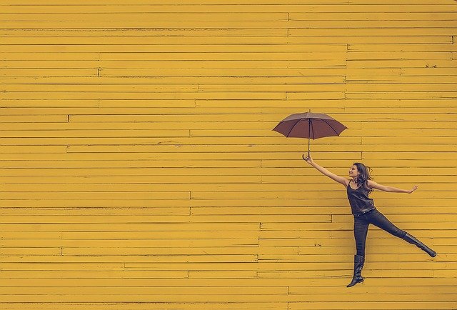 黄色い壁を背景に傘を持ってジャンプする女性