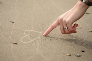 結婚指輪をした左手で砂浜にハートを書く